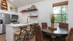 Une cuisine dotée d’un îlot central, de tabourets de bar, d’une table à manger avec des chaises et d’une fenêtre donnant sur la verdure.