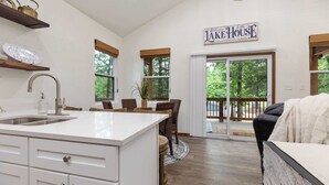 Une cuisine moderne avec un îlot central, un coin repas avec des chaises en osier et une pancarte indiquant : « Bienvenue à la maison au bord du lac ».