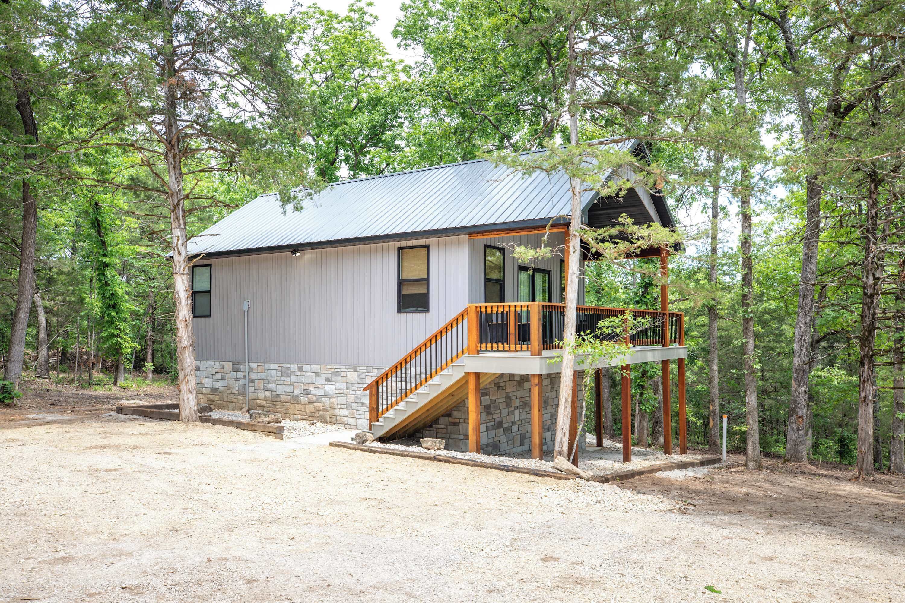 A cabin with a stone foundation, a metal roof, and a wooden staircase leading to a deck.