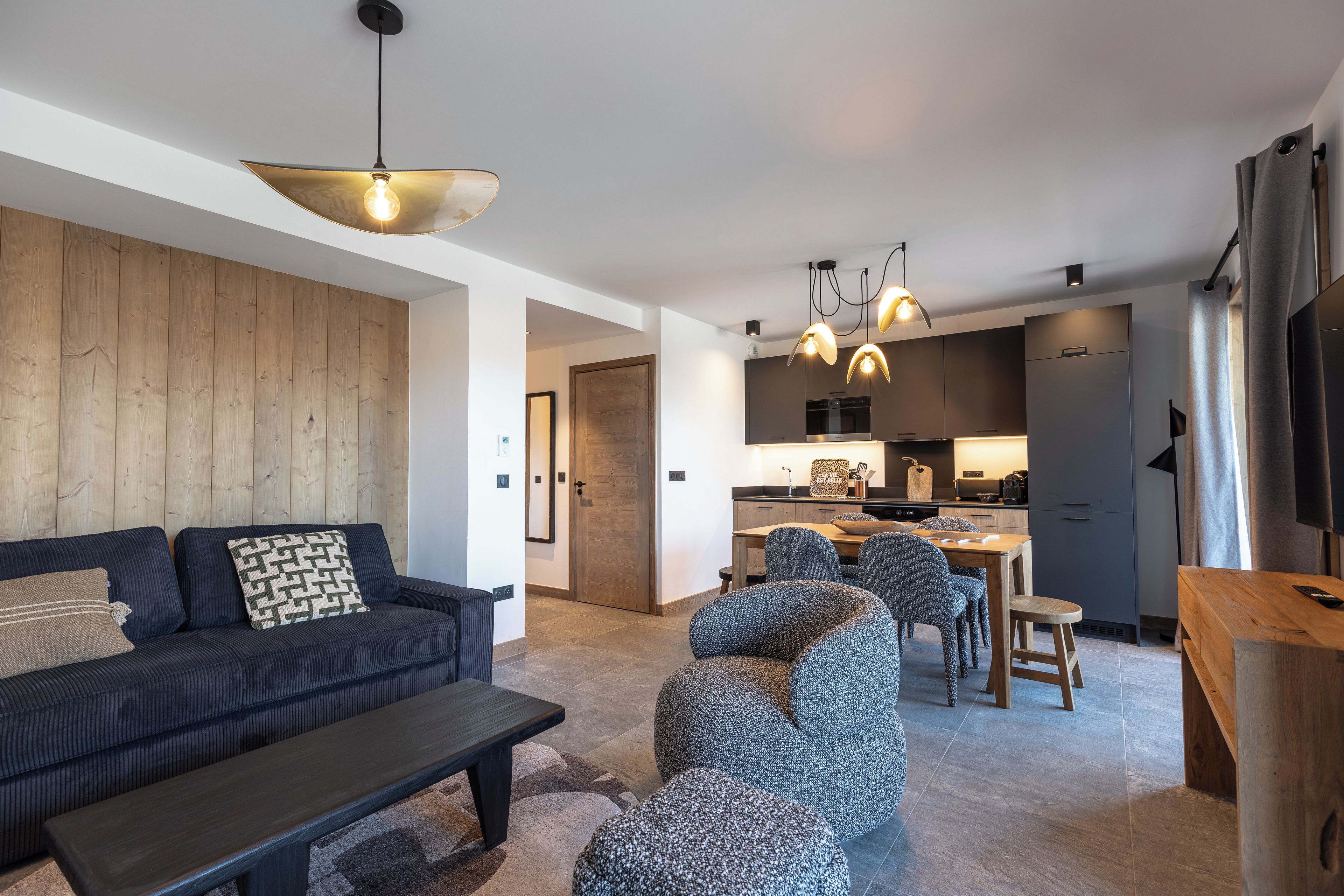Un salon moderne avec un canapé, une table basse et des fauteuils à motifs. Il y a également un coin cuisine avec une table à manger et des chaises.