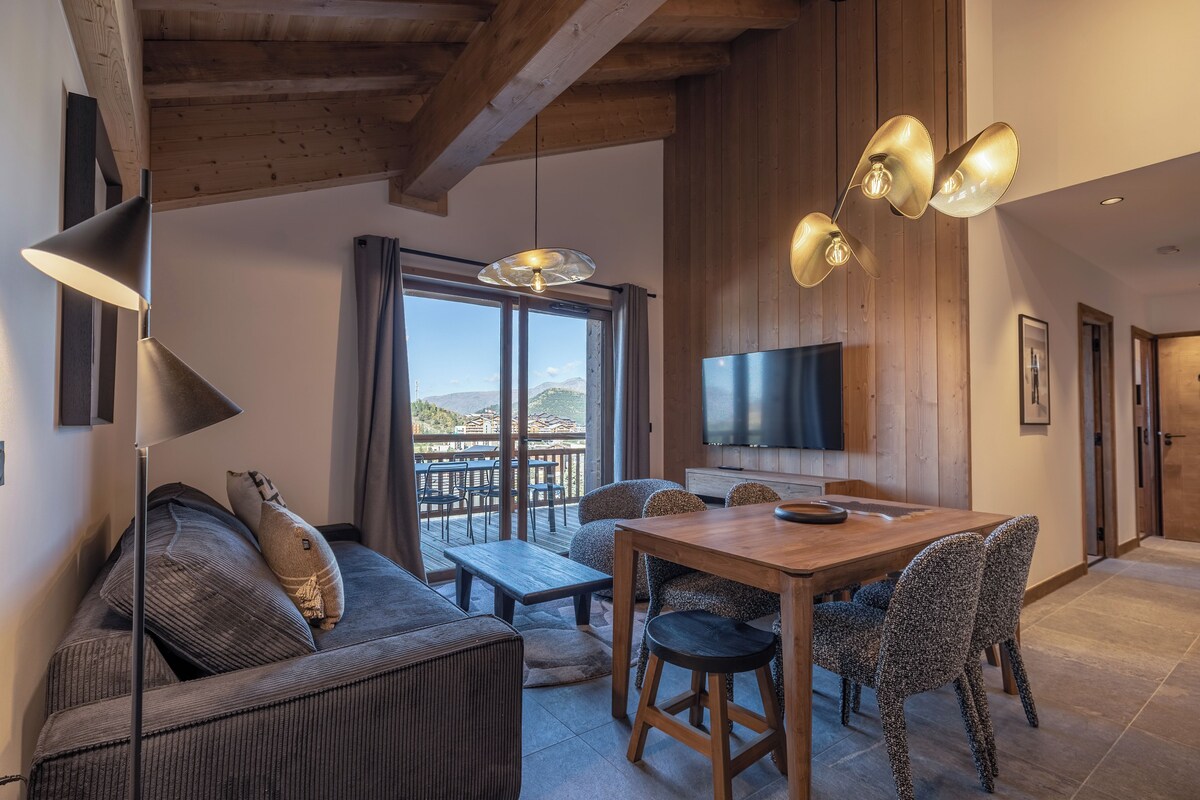 A modern living room with a wooden ceiling, a large TV, and a dining area with a wooden table and patterned chairs.