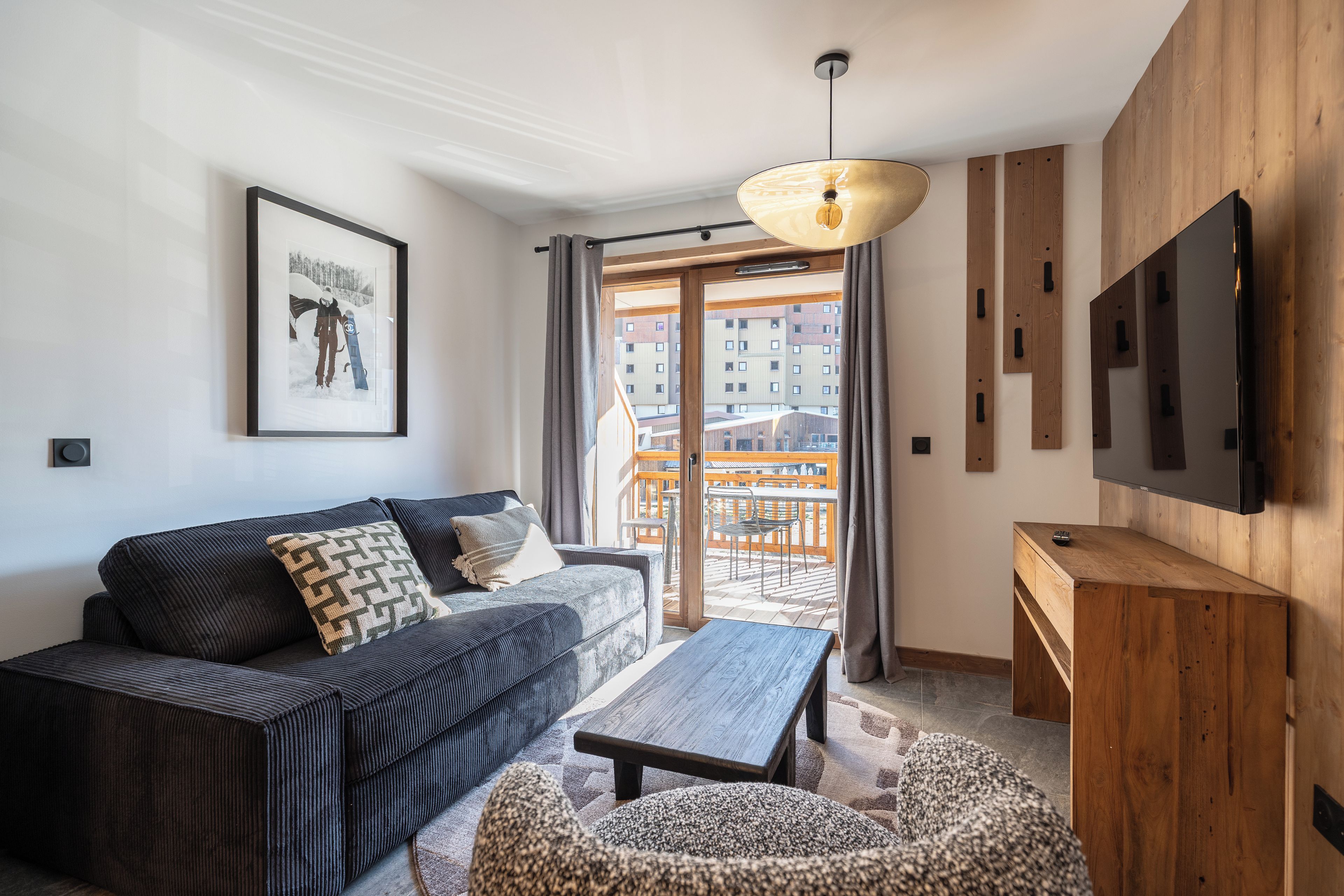 A modern living room with a sofa, a coffee table, a TV, and a balcony with a view of buildings.