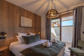 A bedroom with a wooden headboard, a bed with white and green bedding, a hanging light fixture, and a view of a balcony. - TERRESENS - La Perle d'Alba (Huez)