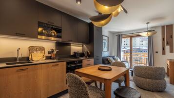 A modern kitchen with a built-in oven, a dining area with a wooden table and patterned chairs, and a view of the city through large windows.