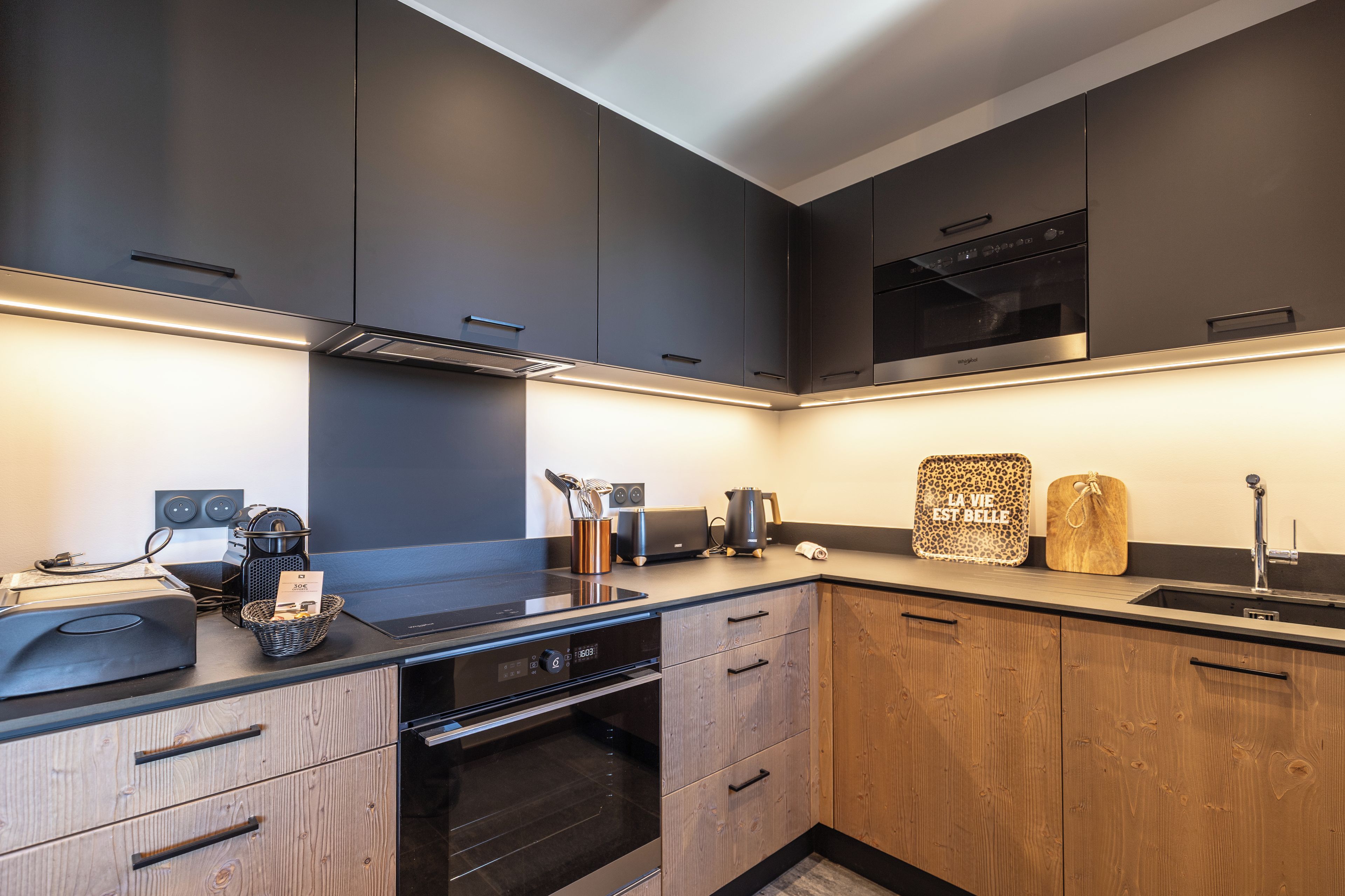 A modern kitchen with dark cabinetry, a built-in oven, and a stainless steel range hood.