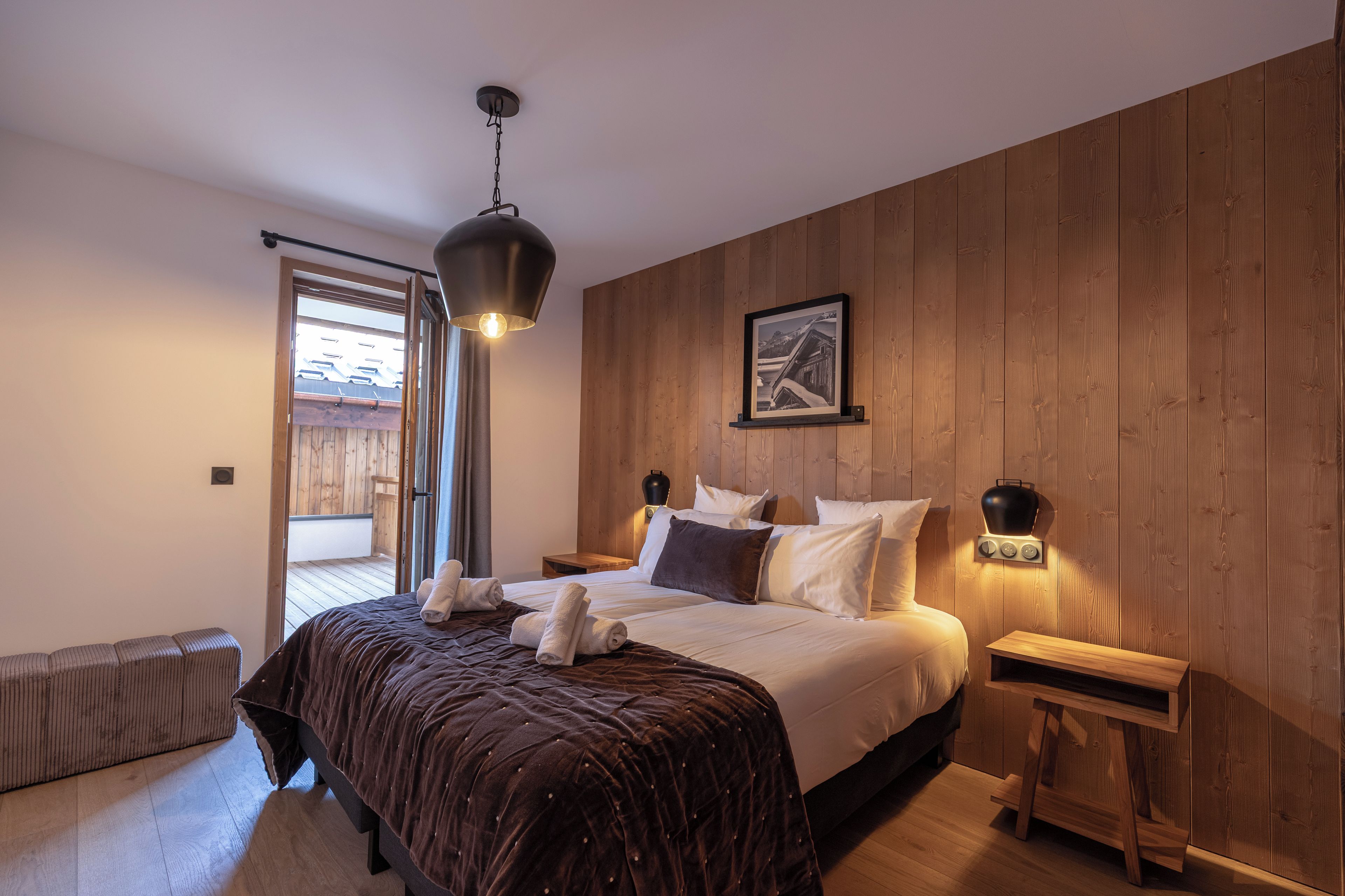 A bedroom with a bed, bedside tables, a wall-mounted light, a picture, and a window.
