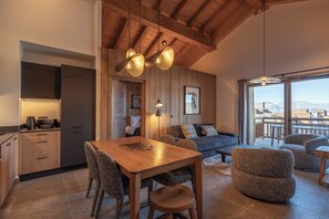 A modern interior with a wooden ceiling, a dining area with a table and chairs, a sofa, and a view through a large window. - TERRESENS - La Perle d'Alba (Huez)