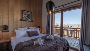 A hotel room with a large bed, a mounted picture, a hanging light fixture, and a balcony with a view of mountains.