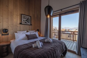 A hotel room with a large bed, a mounted picture, a hanging light fixture, and a balcony with a view of mountains. - TERRESENS - La Perle d'Alba (Huez)