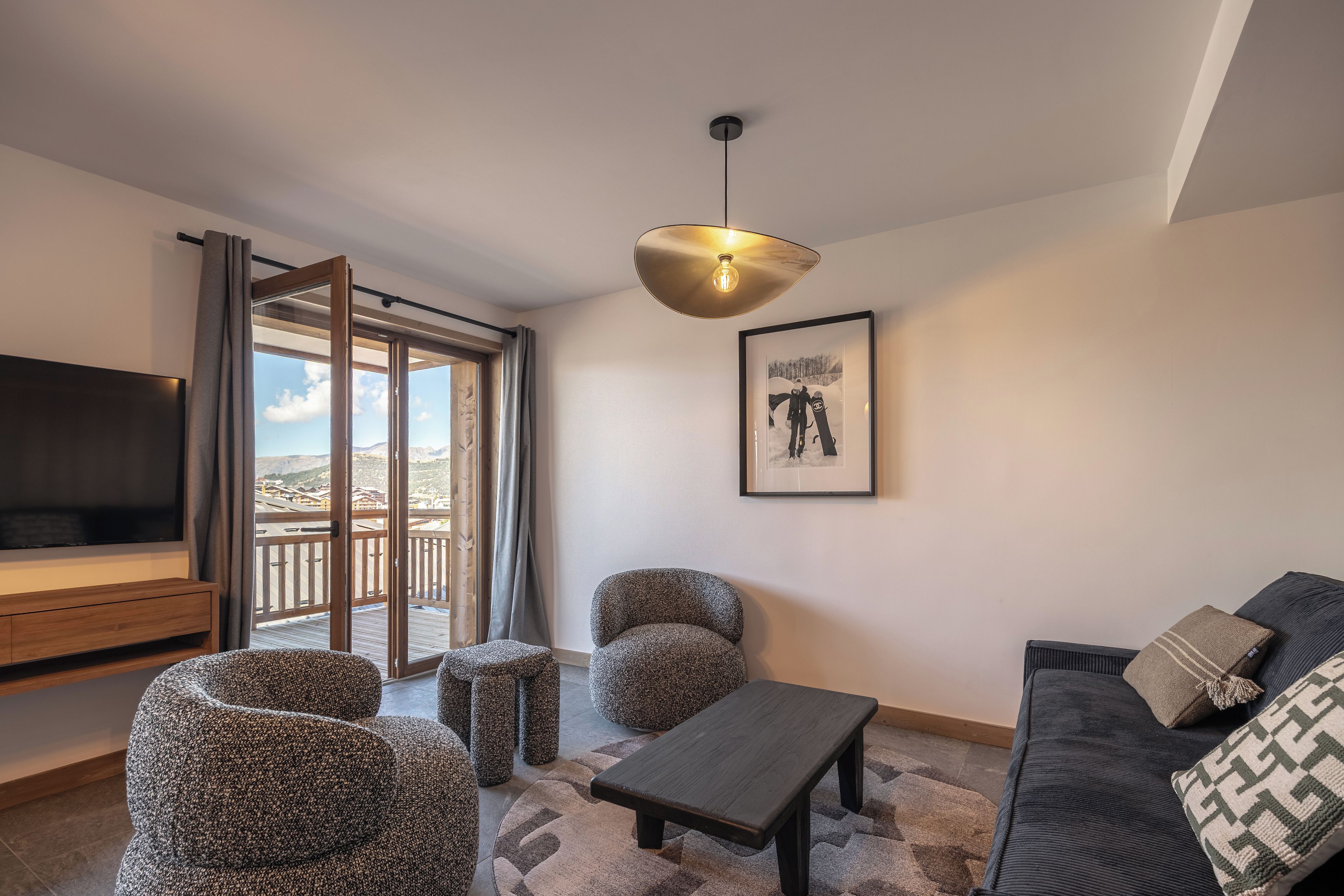 Una sala de estar moderna con televisor, asientos, un cuadro enmarcado y un balcón con vistas.