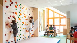 A climbing wall with colorful holds, a padded floor, and a window with natural light. - TERRESENS - La Perle d'Alba (Huez)