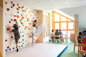 A climbing wall with colorful holds, a padded floor, and a window with natural light.