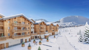 A wooden chalet-style hotel with balconies, a ski slope in the background, and snow-covered ground. - TERRESENS - La Perle d'Alba (Huez)