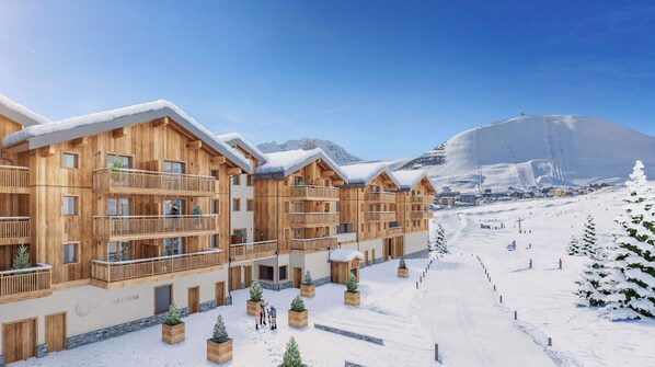 A wooden chalet-style hotel with balconies, a ski slope in the background, and snow-covered ground.