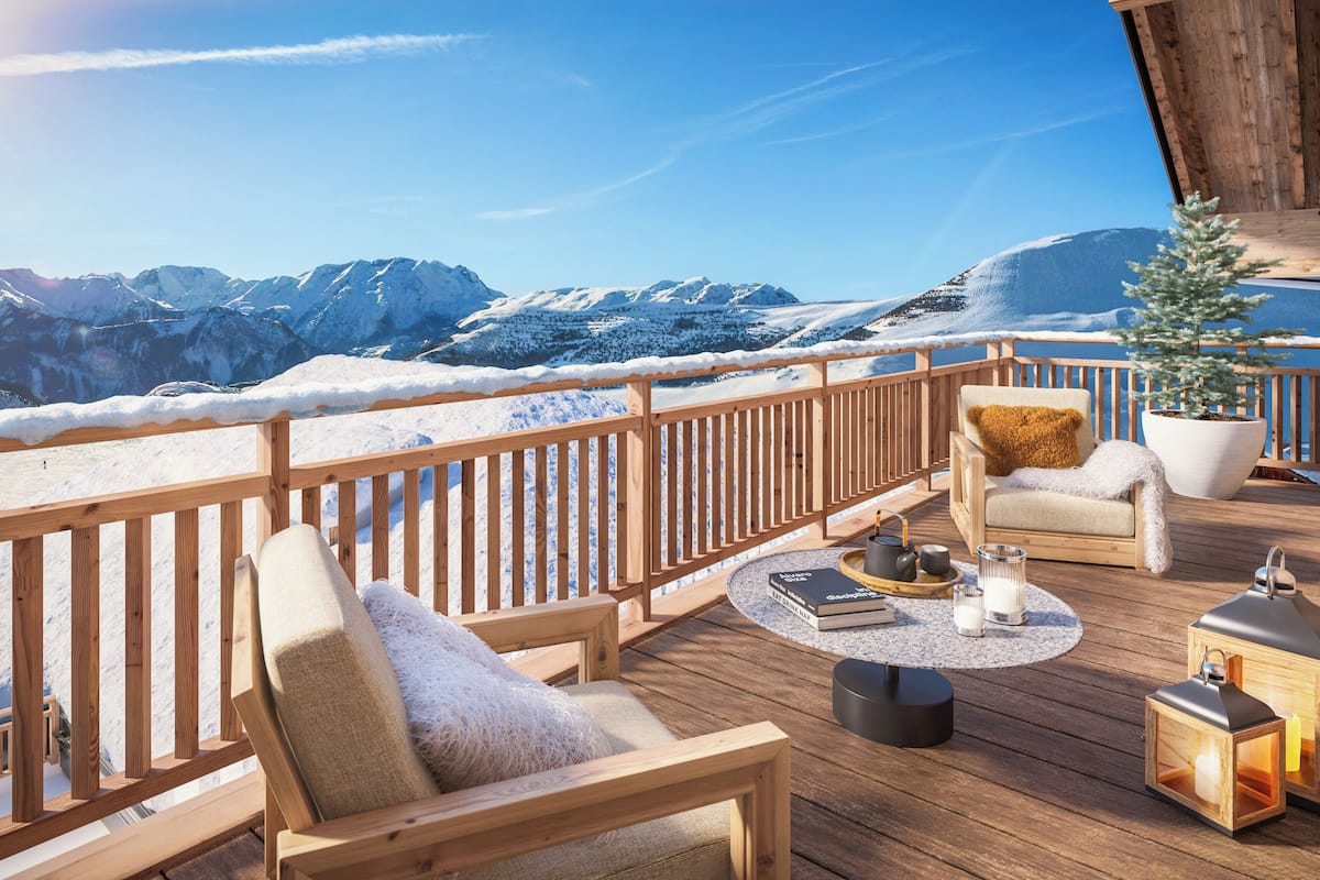 A wooden deck with a view of snow-covered mountains, a chair with a cushion, a small potted plant, and two lanterns.