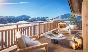 A wooden deck with a view of snow-covered mountains, a chair with a cushion, a small potted plant, and two lanterns.