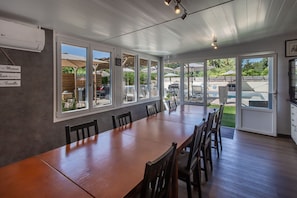 Un comedor amplio con una larga mesa de madera y sillas, ventanas grandes y un patio exterior con sombrillas.