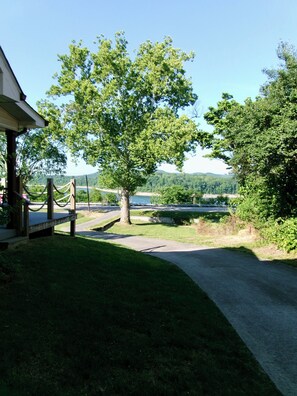 A paved path leading to a building with a porch, surrounded by greenery and a view of a lake. - Louie's Front Porch (Burnside)