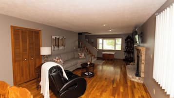Un salon comprenant un canapé, un fauteuil massant, une cheminée et un escalier menant à un autre niveau.