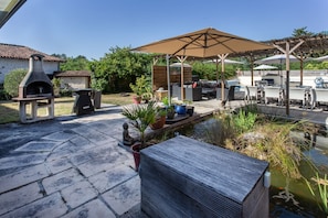 Une terrasse avec des meubles d’extérieur, un barbecue et un petit étang.