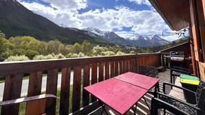 A wooden deck with a red table and chairs, overlooking a mountainous landscape with a clear sky. - Bright family apartment with magnificent views (Le Monêtier-les-Bains)