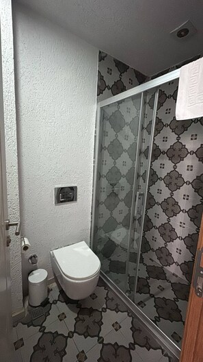A bathroom with a toilet, a shower with patterned tiles, and a door with a towel hanging on it. - Taksim Square - Deluxe Studio 301 (Istanbul)