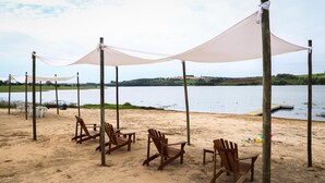 A beach with wooden chairs and a canopy, overlooking a calm body of water. - Quinta dos Cambaras Ecopousada (Itaí)