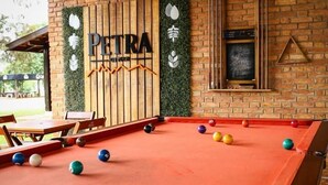 A billiards table with balls, a wooden sign with 'Petria' on it, and a brick wall with a hanging light fixture. - Quinta dos Cambaras Ecopousada (Itaí)