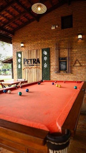 Une table de billard avec des billes, un panneau en bois portant lâinscription « PETRA » et un motif reprĂ©sentant une montagne, et un mur de briques avec un tableau noir.