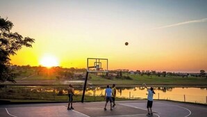 A basketball court with a hoop, surrounded by a body of water and trees, during sunset. - Quinta dos Cambaras Ecopousada (Itaí)