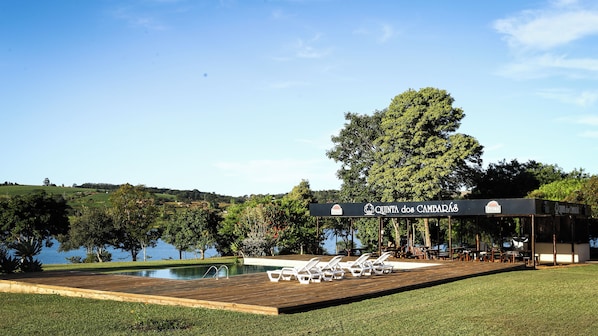 Un espace piscine avec des chaises longues, une terrasse en bois et un panneau indiquant lâentrĂ©e de Quinta dos CambarĂĄ.