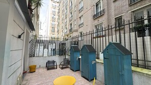 Une cour avec un sol carrelé, un objet circulaire jaune et des dépendances bleues.