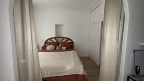 Ein schmales Zimmer mit einem Bett, einem Kleiderschrank und einer Tür.