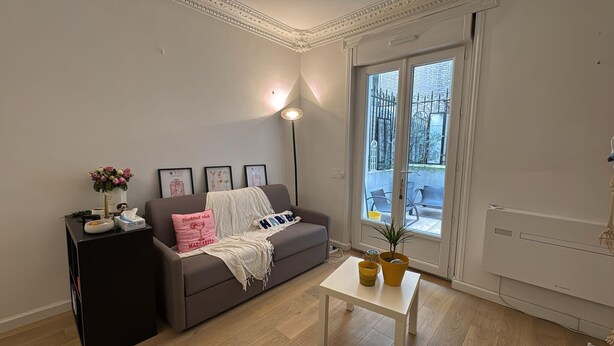 Un salon comprenant un canapé, une petite table, un lampadaire et une fenêtre donnant sur un espace extérieur aménagé pour s’asseoir.