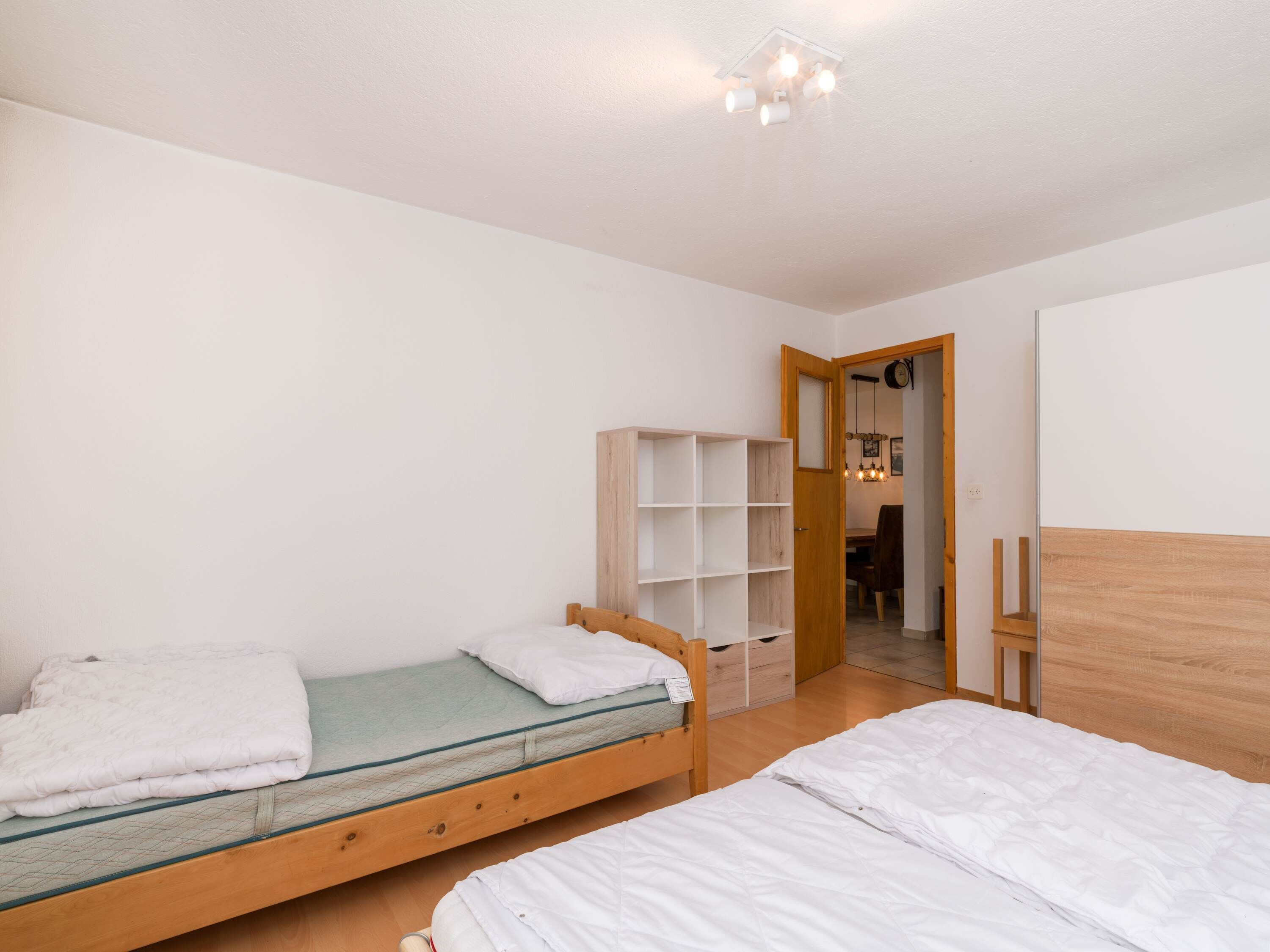 A bedroom with two beds, a wooden wardrobe, and a door leading to a bathroom.