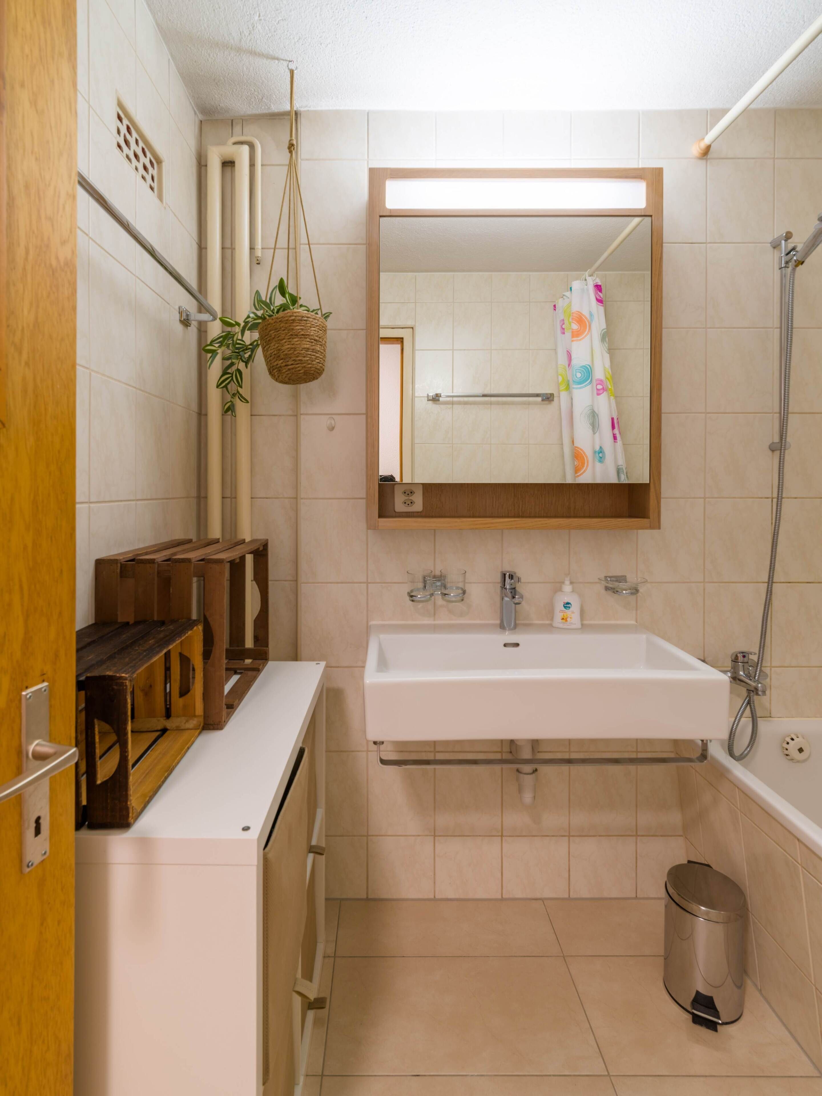 Een badkamer met een wit wastafel, spiegel, douche en een prullenbak.
