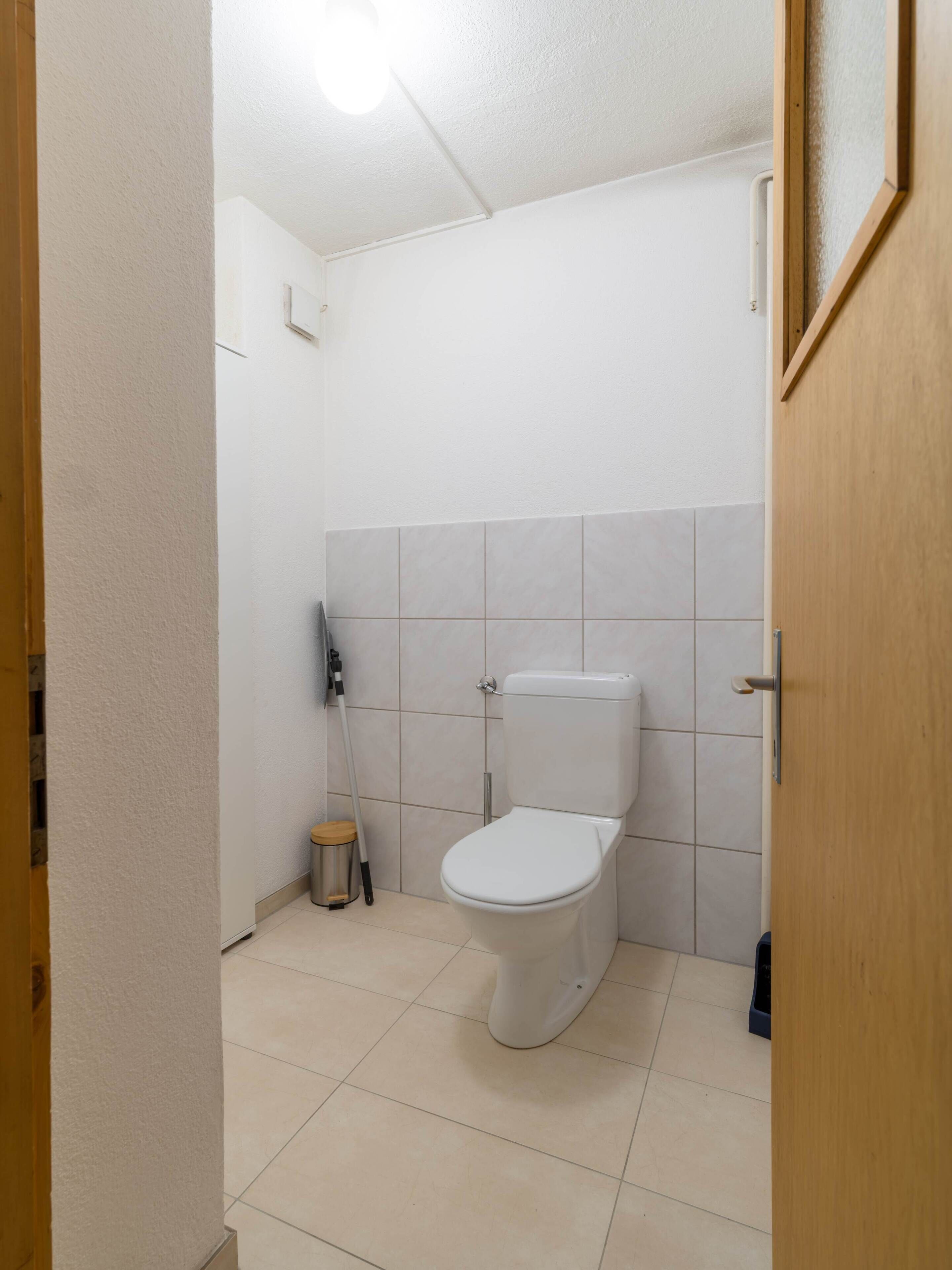 A small, clean bathroom with a toilet, a hand dryer, and a trash bin.