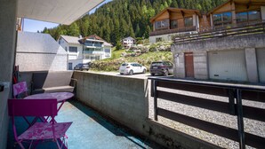 Un balcone con vista su un pendio boscoso, un'area di parcheggio con auto e un edificio con facciata in legno.