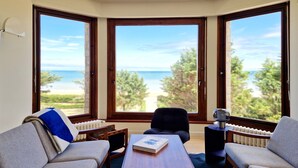 A room with a view of the sea, a sofa, a table, and a chair.