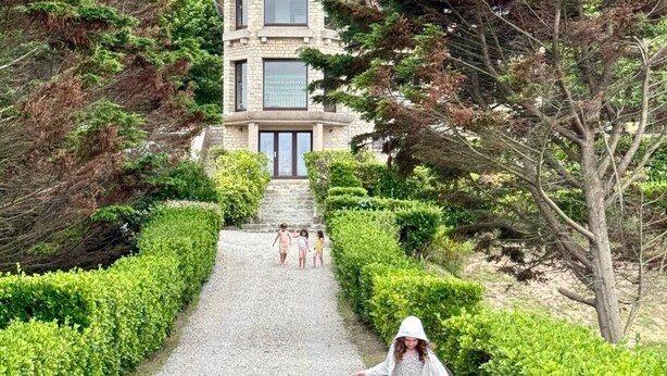 A pathway leading to a building with a stone facade and a red roof, surrounded by greenery.