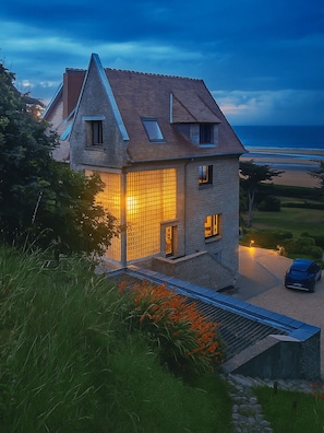 A two-story house with a sloped roof, a large glass window, and a car parked in the driveway.