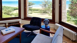 A room with a view of the sea, a black chair, a white sofa, a table with a book, and a decorative globe.
