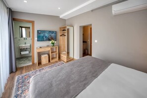 Ein Hotelzimmer mit Bett, Schreibtisch mit Stuhl, Fernseher, Kleiderschrank und einem durch eine offene Tür einsehbaren Badezimmer.