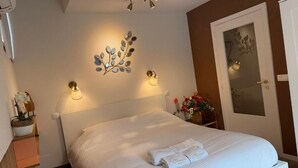 A neatly made bed with a white comforter and folded towels, a decorative wall art piece, and a wall-mounted light fixture. - Clemanbruges (Bruges)