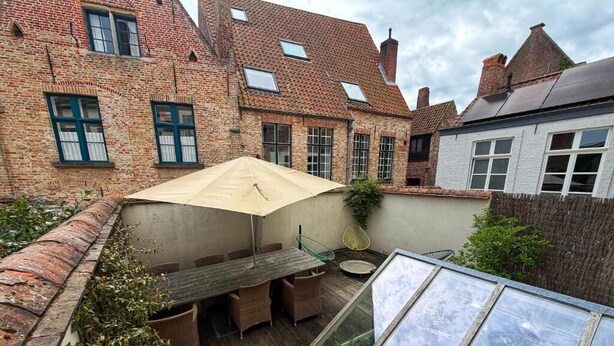 A courtyard with a wooden table and chairs, a glass enclosure, and a brick building with windows. - Clemanbruges (Bruges)