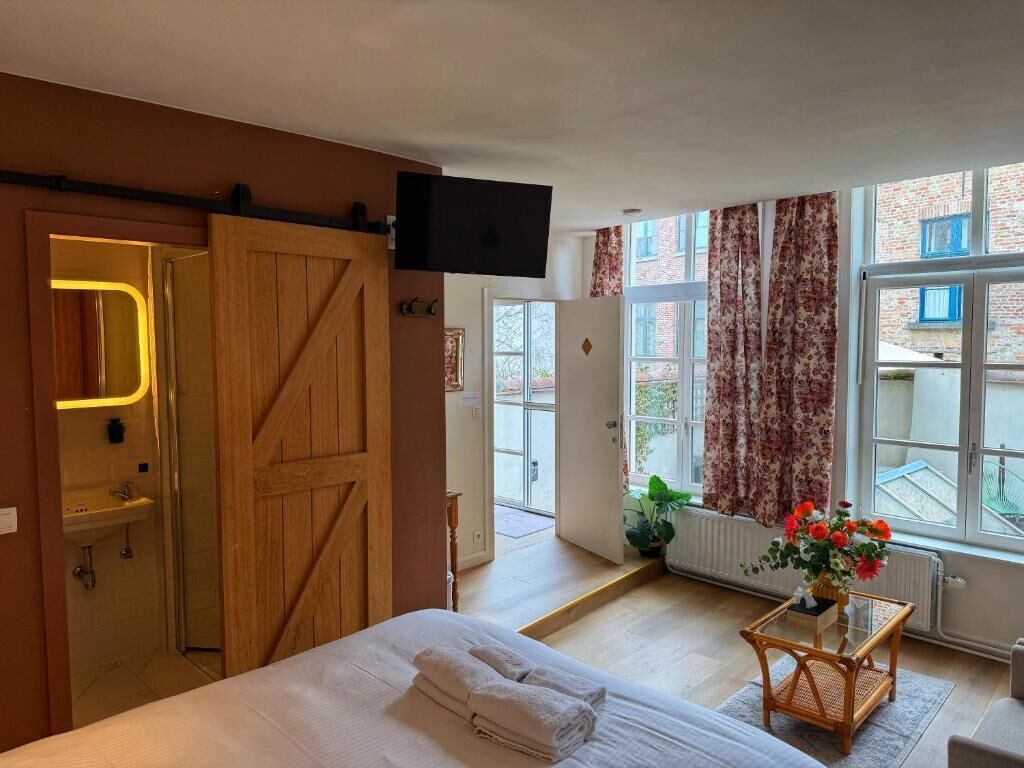 A bedroom with a bed, a wooden wardrobe, a television, a window with curtains, and a view of the street.