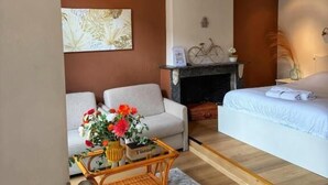 A room with a sofa, a bed, a wicker coffee table with flowers, a fireplace, and a wall-mounted TV. - Clemanbruges (Bruges)