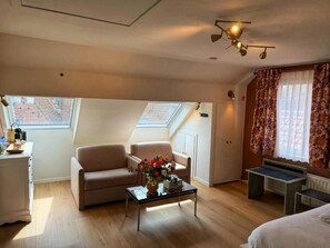 Una habitación con sofá, una mesa baja con flores, un escritorio y una cama.