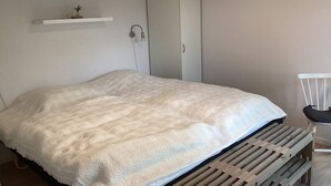 Quarto com cama, guarda-roupa, prateleira com uma planta e uma cadeira.