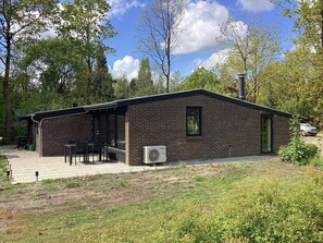 Ein Backsteinhaus mit überdachter Terrasse, Außenbestuhlung und Klimaanlage.